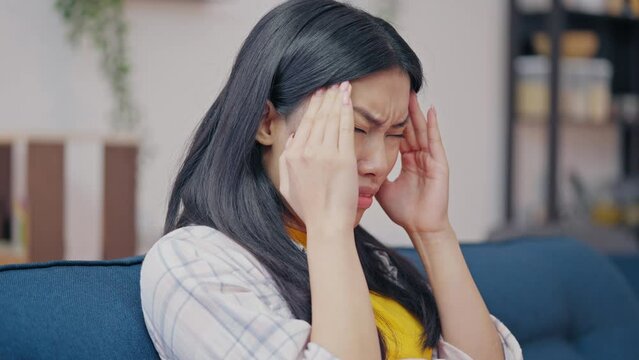 Sad Asian woman suffering from migraine, massaging temples, disease symptom