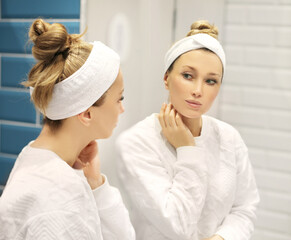 Obraz premium woman looking in the mirror in the bathroom and taking care of her skin.Applying the cream..Magic anti-aging cream.