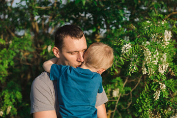 Father's Day. Father and son are playing and hugging on a green background of foliage and acacia. Happy family.