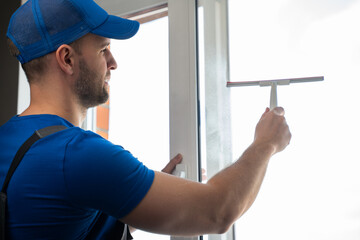 Worker in blue uniform cleans plastic window with detergent and squeegee. Soapy stains on window...