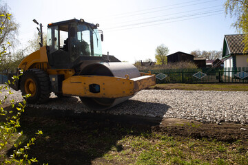 The roller rolls the gravel preparing the soil for the road. Rural road repairs in Kazakhstan.