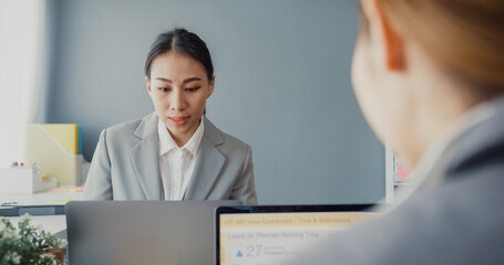 Obraz premium Young asia businesswomen using laptop on table working and communicate sitting on office desk at workplace. Remote webinar, internet technology, lifestyle social distancing and work after coronavirus.