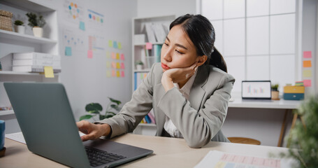 Young Asian businesswoman sit on desk with laptop overworked tired burnout syndrome at office. Exhausted lady with sleeply eye at workplace, Girl not enjoy unhappy with work, Work mental health. - obrazy, fototapety, plakaty