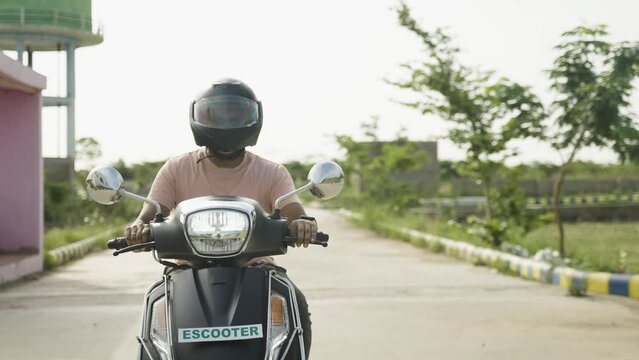 front view tracking shot of young Man driving Ev or electric scooter by wearing helmet on road showing with copy space - concept of safety, technology and sustainable lifestyle