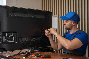 Master in blue T-shirt smiles after repairing TV set connector with screwdriver sitting at table....