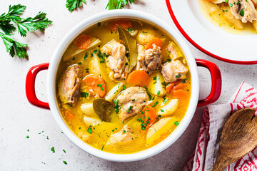 Chicken stew with potatoes and carrots in red saucepan. Chicken soup with vegetables and herbs....