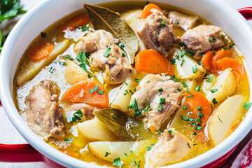 Chicken stew with potatoes and carrots in red saucepan. Chicken soup with vegetables and herbs. Comfort food recipe. - obrazy, fototapety, plakaty