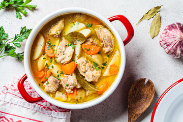 Chicken stew with potatoes and carrots in red saucepan. Chicken soup with vegetables and herbs....