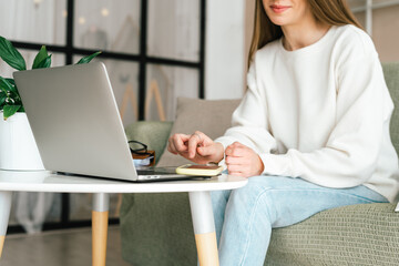 Fototapeta premium Freelance young woman with mobile cellphone typing at laptop and working from home office with. Happy girl on workplace at desk. Distance learning online education. Taking selfie or video chat