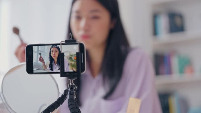 Asian beauty blogger applying make-up on smartphone camera, testing cosmetics