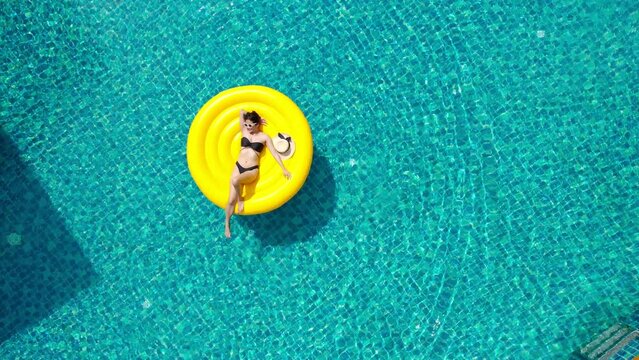 Beautiful young asian woman with yellow inflatable ring relaxing in swimming pool. top view