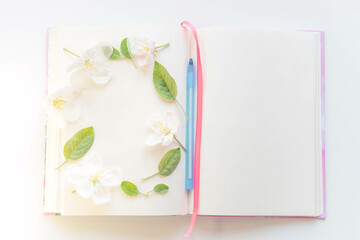 Open book with white sheets and a blue pen in apple blossoms around