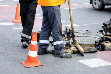 Workers repair the road surface, man with shovel near the sewer manhole. Construction and repairing...