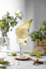 Pear cocktail with pear puree and fresh fruit and flowers on light gray background. Summer cold pear drink lemonade with ice on the table, Sparkling Mocktail dessert beverage with flowering twigs