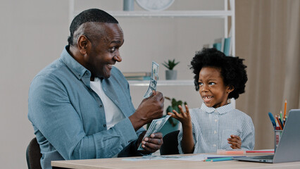 African american father helps to do homework teaches little daughter arithmetic using dollar bills...