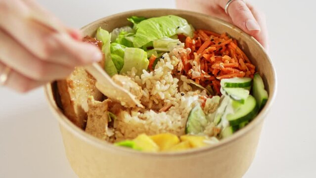 Hands taking food from asian poke vegan bowl with rice, avocado, tofu and salad. Healthy vegetarian delivery meal.