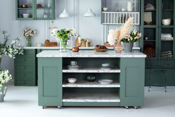 Green kitchen interior with furniture. Stylish cuisine with flowers in vase. Wooden kitchen in...