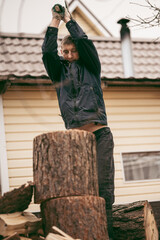 A man with a heavy axe in his hands. An axe in the hands of a lumberjack chopping or chopping tree trunks. A man is chopping firewood in the yard of a house in the village