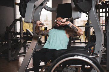 A middle-aged person in a wheelchair training in a gym, working his pecs. Sports overcoming concept.