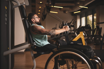 Fototapeta na wymiar A middle-aged person in a wheelchair training in a gym, working his pecs. Sports overcoming concept.