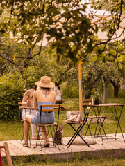 Fototapeta premium Women and a cat in a summer terrace. Cafe terrace in a garden. Sunny summer day. Friends in a cafe. Breakfast, lunch or brunch with friends. 