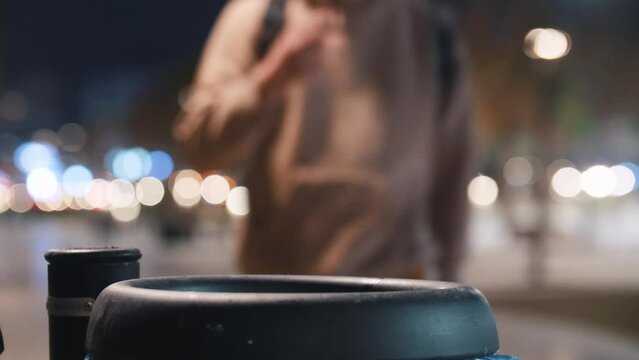 A young man walks to the garbage can and throws a cigarette butt at it