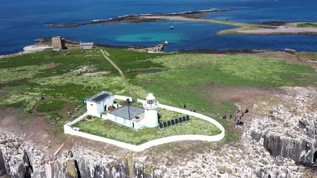 Aerial footage of the seaside coastal town of the village of Seahouses in the UK showing The Farne Lighthouse, a lighthouse on the southern tip of Inner Farne. Built in the early 19th century.