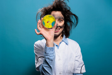 Crazy scientist with dirty face and messy hair with petri dish glass plate having dangerous...