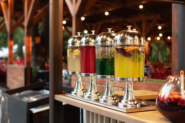 Glass jars with refreshing lemonade at summer party, cocktail bar. Soft selective focus. Big glass jars with tap filled with fresh cold drinks served in bar. Event with catering. Sangria cocktail