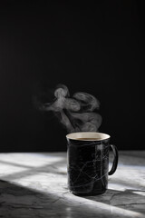 The cap of hot coffee with steam on the marble table