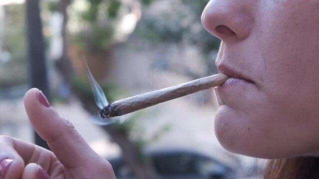 woman smoking outside. lady taking a drag from the cigarette white smoke in the air. getting high. taking a break. taking a puff from a join. slow motion. close up of mouth