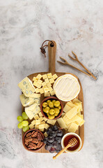 Party cheese board with a variety of cheese, grape, nuts, olives, and honey on a kitchen plate