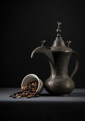 Antique arabic coffee pot. Coffee beans are spilling out from a cup. Photo of Arabic Dallah.