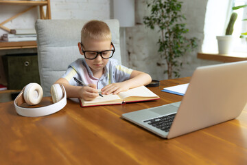One cute little boy, school age kid listening online lesson, using laptop at home interior. Education, childhood, people, homework and school concept.