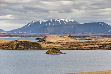 View across a lake towards a small island, a pseudocrater and a mountain range in the Myvatn area in Iceland