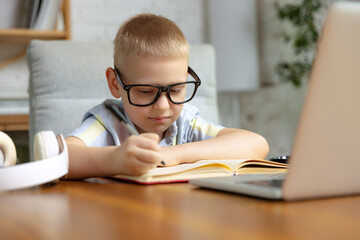 Little boy, school age kid doing homework, using laptop at home interior. Education, childhood, people, homework and school concept.