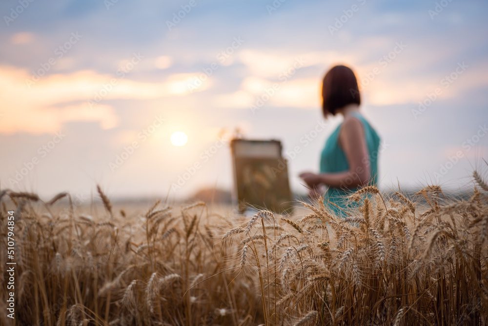 Wall mural Golden ripe wheat and an artist painting on the background. Focus on the foreground with bright spikelets