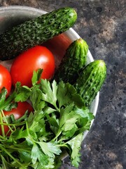 Cucumber, tomato and parsley. Fresh vegetables in a rustic metal plate on a black concrete background. Summer salad ingredients.
