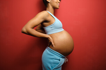 Detail of sporty pregnant woman belly on red wall background.