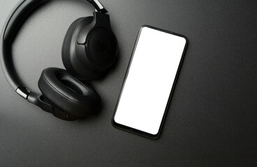 Headphones with smartphone with blank screen on black background. Music app, listening to audio,...
