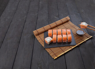 Philadelphia sushi with soy sauce and chopsticks on a black wooden background. Sushi with red fish,...