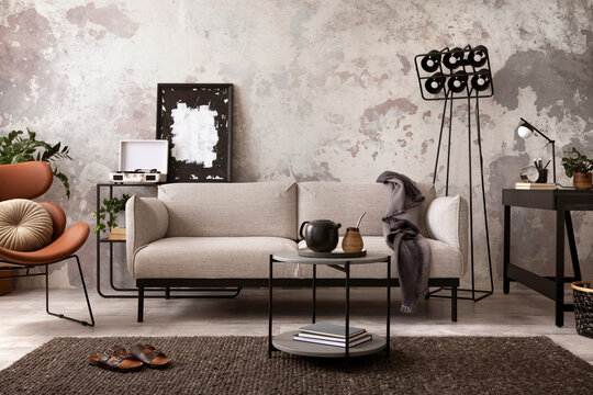 The stylish compostion at concrete living room interior with design gray sofa, wooden coffee table, desk and elegant personal accessories. Loft and industrial interior. Home decor. Template.