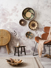 The stylish ethnic composition at living room interior with design brown armchair, colorful baskets, coffee table and elegant personal accessories. Grey concrete wall. Cozy apartment. Home decor.