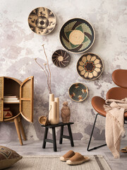 Fototapeta na wymiar The stylish ethnic composition at living room interior with design brown armchair, colorful baskets, coffee table and elegant personal accessories. Grey concrete wall. Cozy apartment. Home decor.