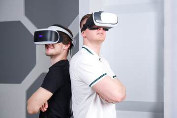 Happy two 2 young handsome men, positive smiling guys using, wearing a modern device virtual reality headset mask or 3D, AR, VR glasses, playing game together. People and technology metaverse concept