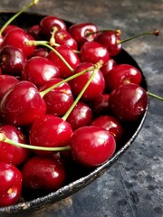 Ripe red cherries on a metal rustic retro plate on a black concrete background. Flatlay with summer fruits and berries.