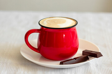 Red cup of cappuccino and chocolate on the table close-up. Food photo.