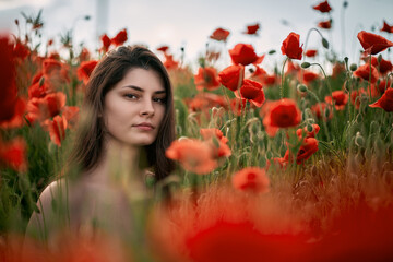 Obraz na płótnie Canvas Beautiful young girl in the red poppy field. Brunette woman with naked shoulders outdoors. Concept of women's relaxation and happiness in the rural nature
