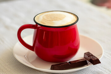 Red cup of cappuccino and chocolate on the table close-up. Food photo.