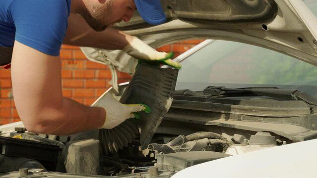 Man in work gloves checks satisfactory state of car engine air filter closeup. Diagnosis of internal spare parts of car and serviceability outdoors